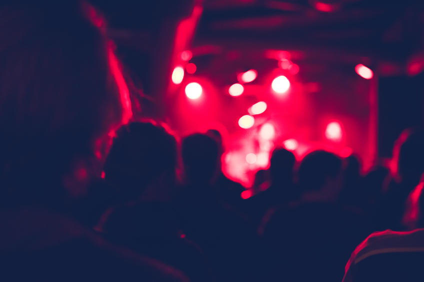 Defocused shot of people cheering on a rock concert. Group of unrecognisable people. Shot from back. The scene is illuminated with red lights.